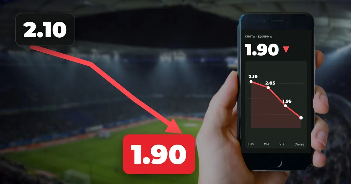 Mano con un celular que muestra una gráfica de una cuota que baja de 2.10 a 1.90, frente a un estadio de noche